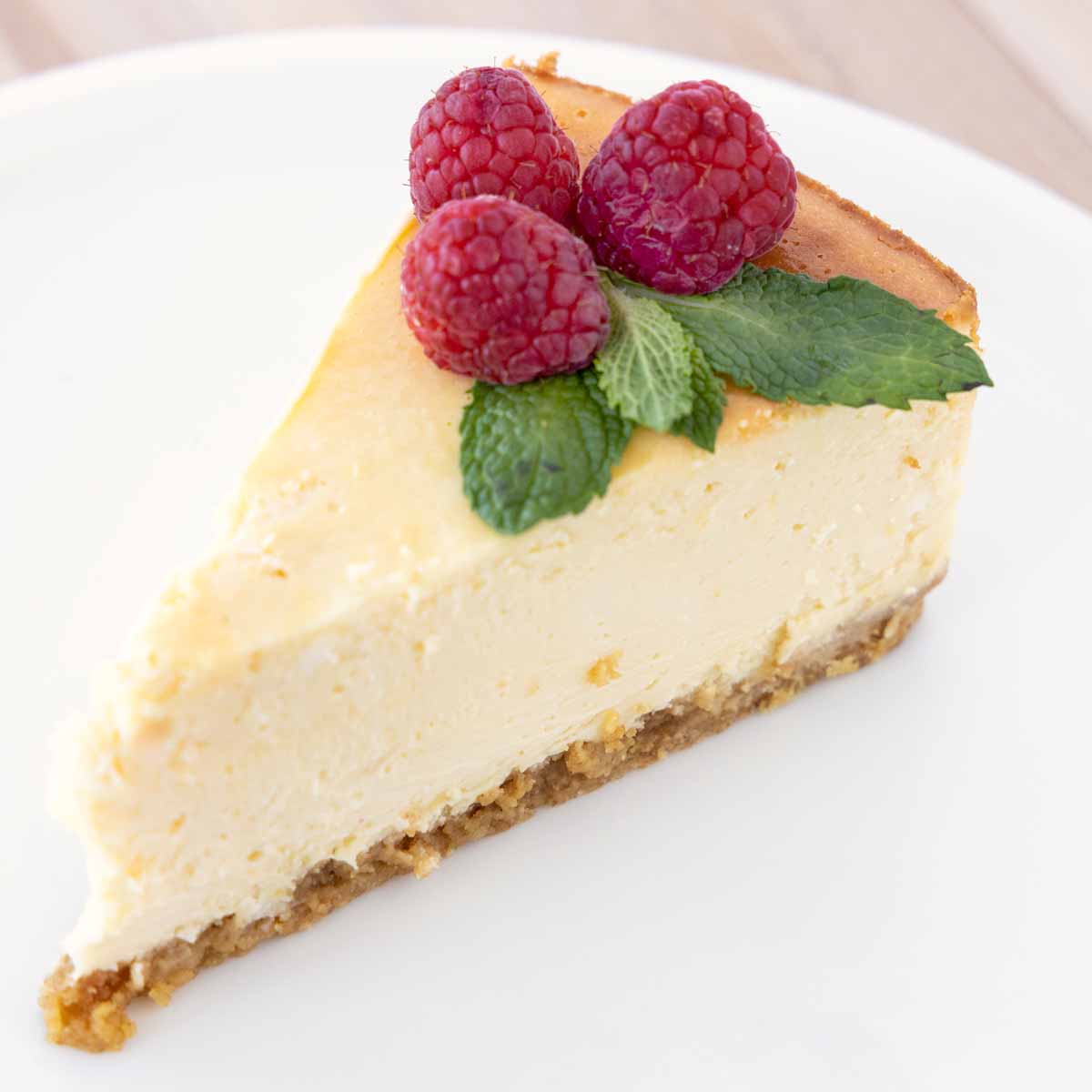 slice of cheesecake with raspberries and mint leaves on a white plate