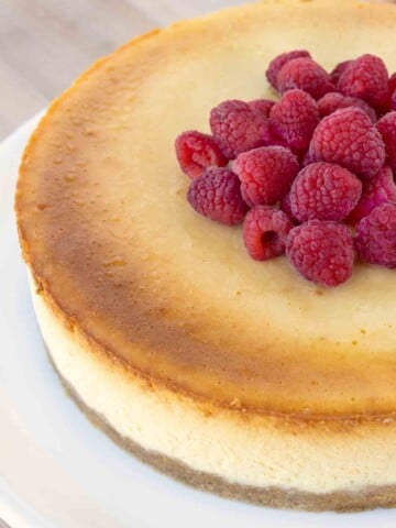 overhead partial view of Chicago style cheesecake with raspberries on a white platter