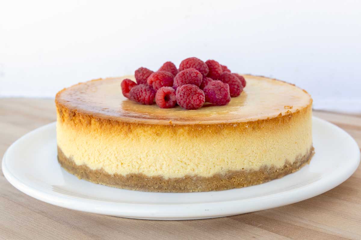 side view of Chicago style cheesecake with raspberries on a white platter