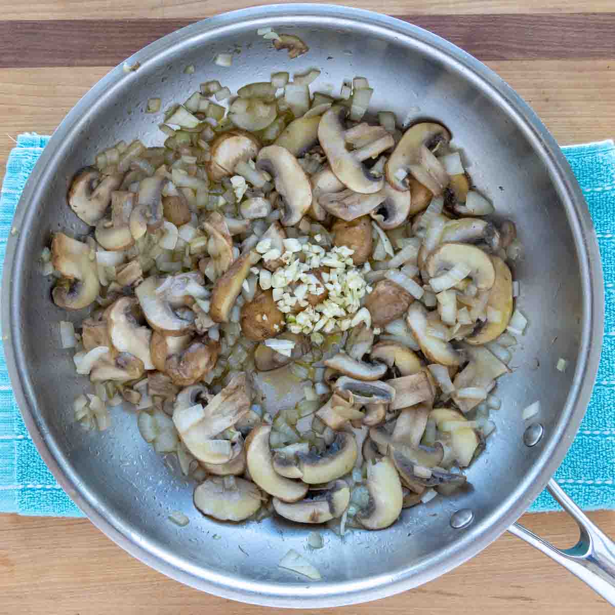 sauteed mushrooms and onions with garlic added to a saute pan