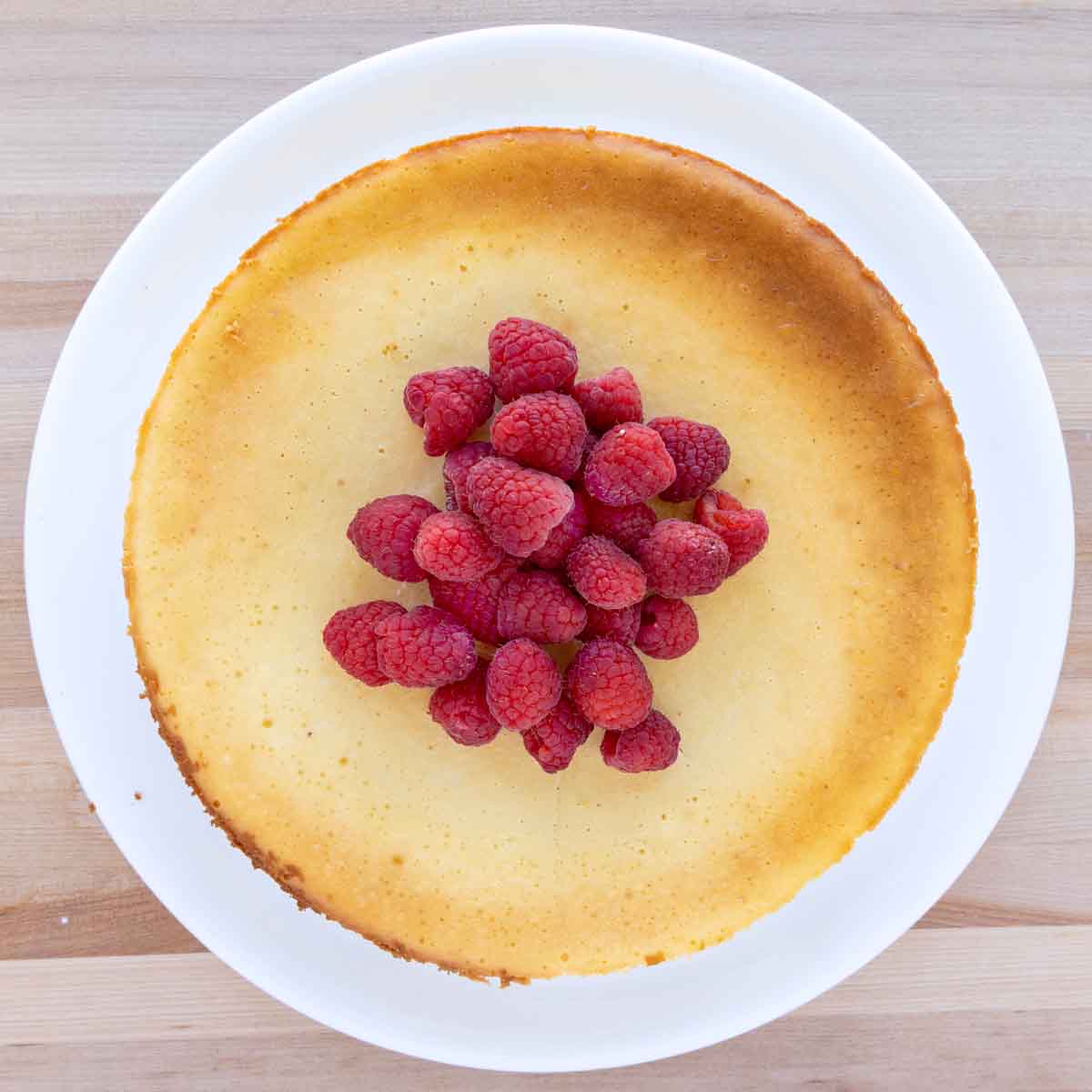 overhead partial view of Chicago style cheesecake with raspberries on a white platter