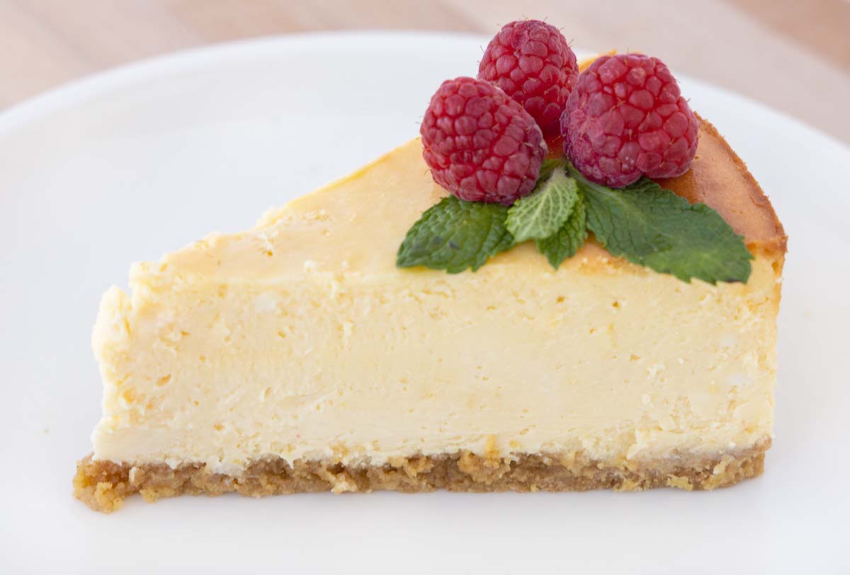 slice of cheesecake with raspberries and mint leaves on a white plate