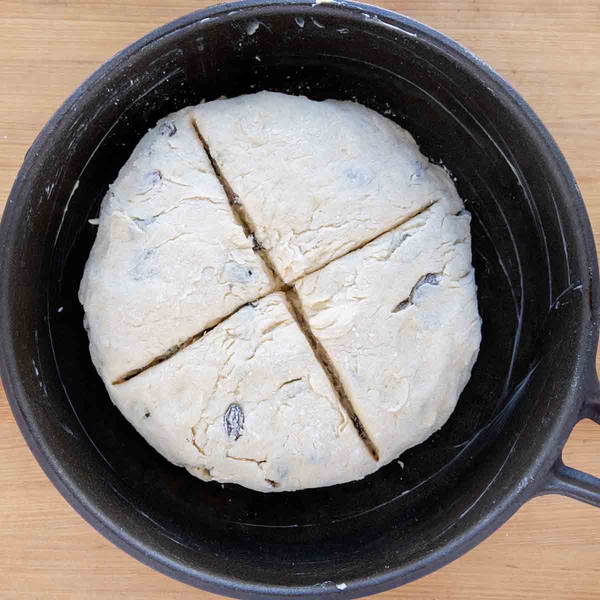 soda bread with an cross cut into the dough in a buttered cast iron pan
