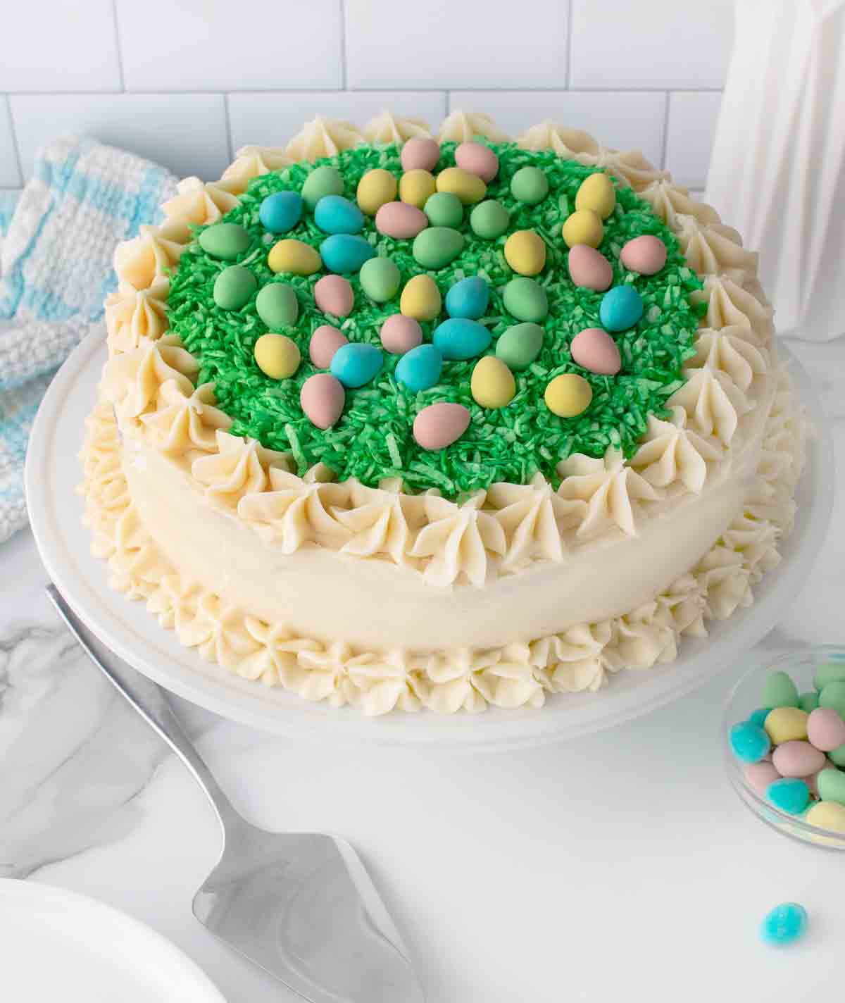 whole decorated Easter cake on a white pedestal with a cake server in the foreground.