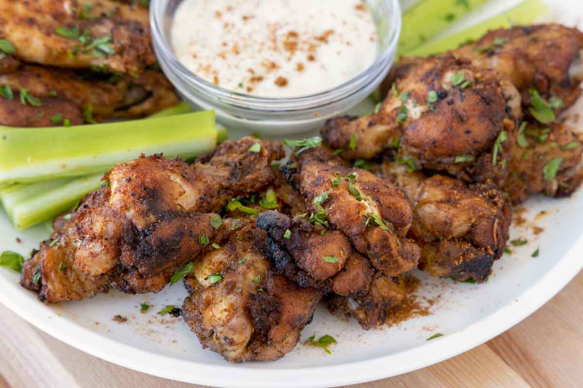 close up of cajun chicken wings on a white plate with celery sticks and bleu cheese dressing