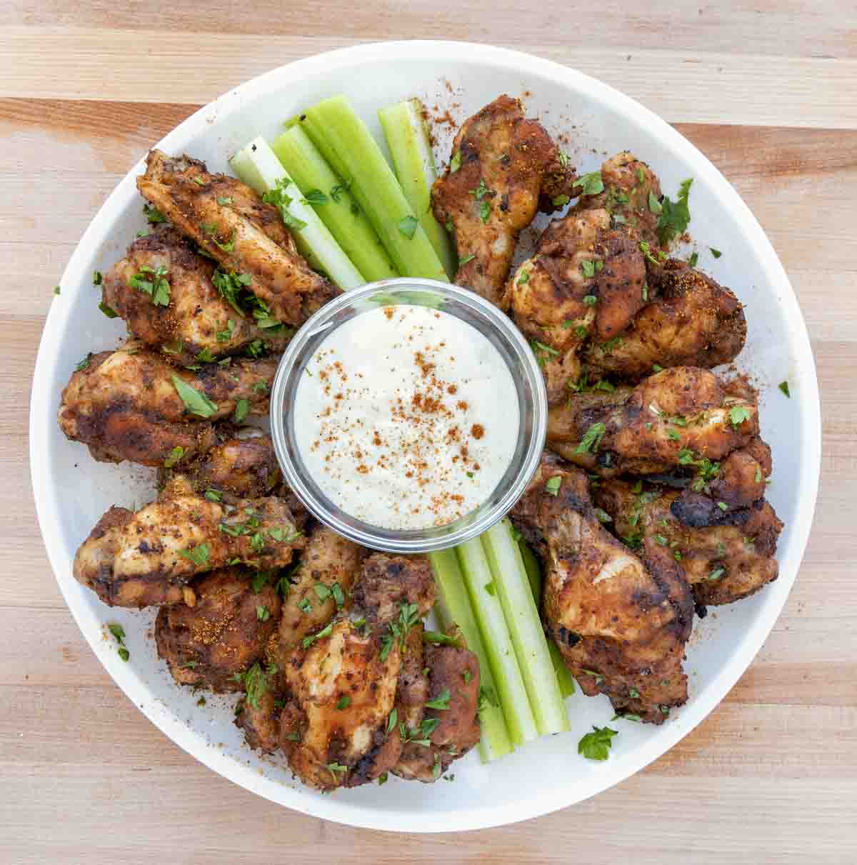 cajun chicken wings on a white plate with celery sticks and bleu cheese dressing
