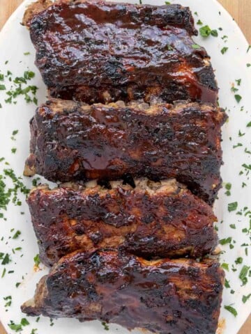 overhead view of barbecued half racks of baby back ribs on a white platter