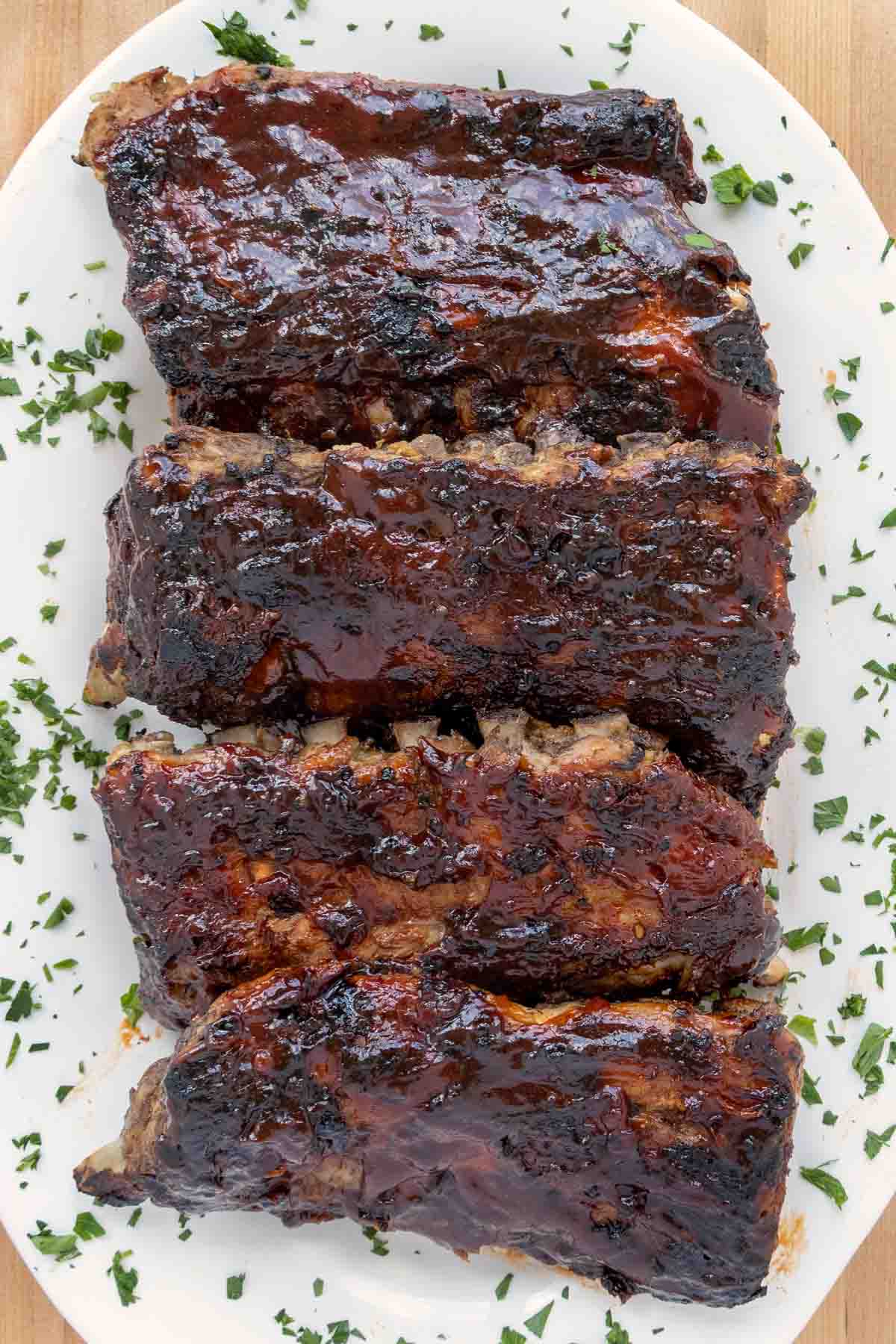 overhead view of barbecued half racks of baby back ribs on a white platter