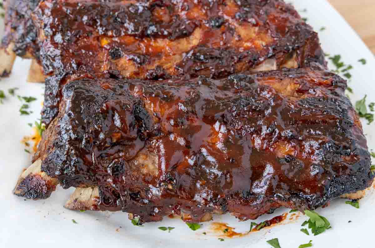 close up of fully cooked ribs coated with barbecue sauce on white platter