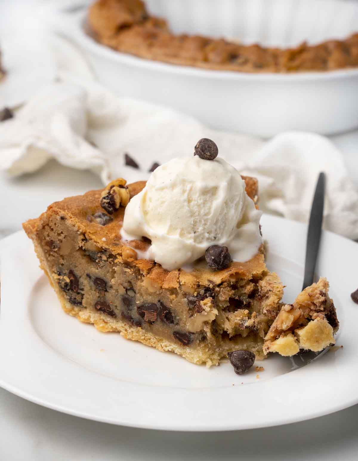 slice of tollhouse cookie pie with ice cream on top and a fork with pie on it