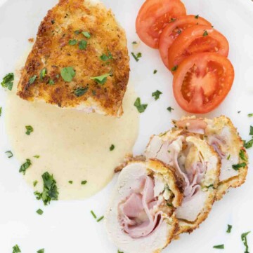 chicken with cordon bleu with slices, dijon sauce and tomato slices on a white plate