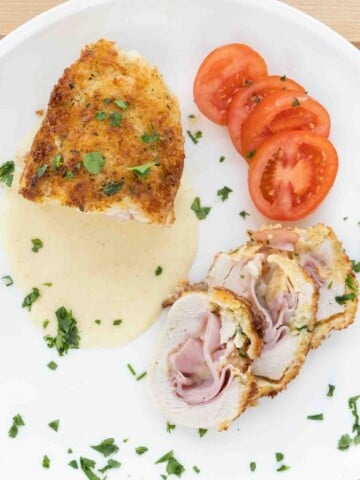 chicken with cordon bleu with slices, dijon sauce and tomato slices on a white plate