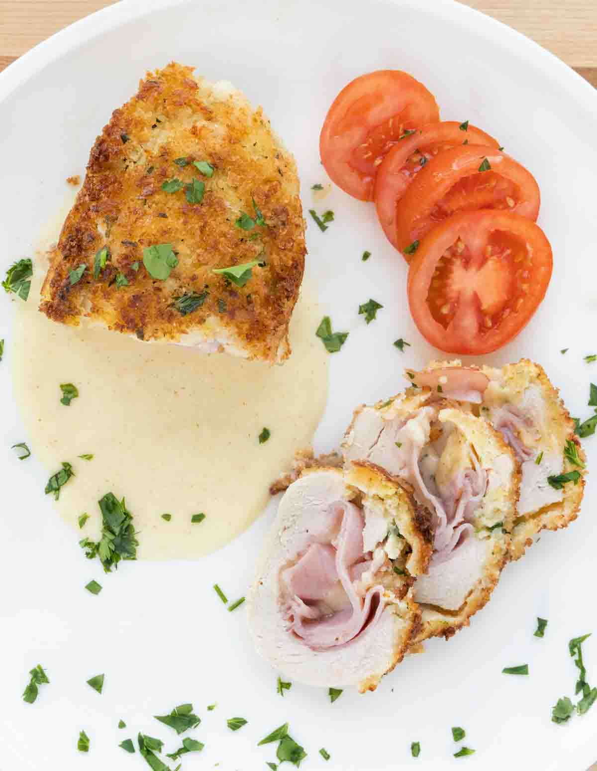 chicken with cordon bleu with slices, dijon sauce and tomato slices on a white plate