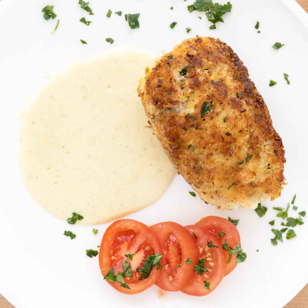 whole chicken cordon bleu on a white plate with the dijon sauce and mini tomato slices