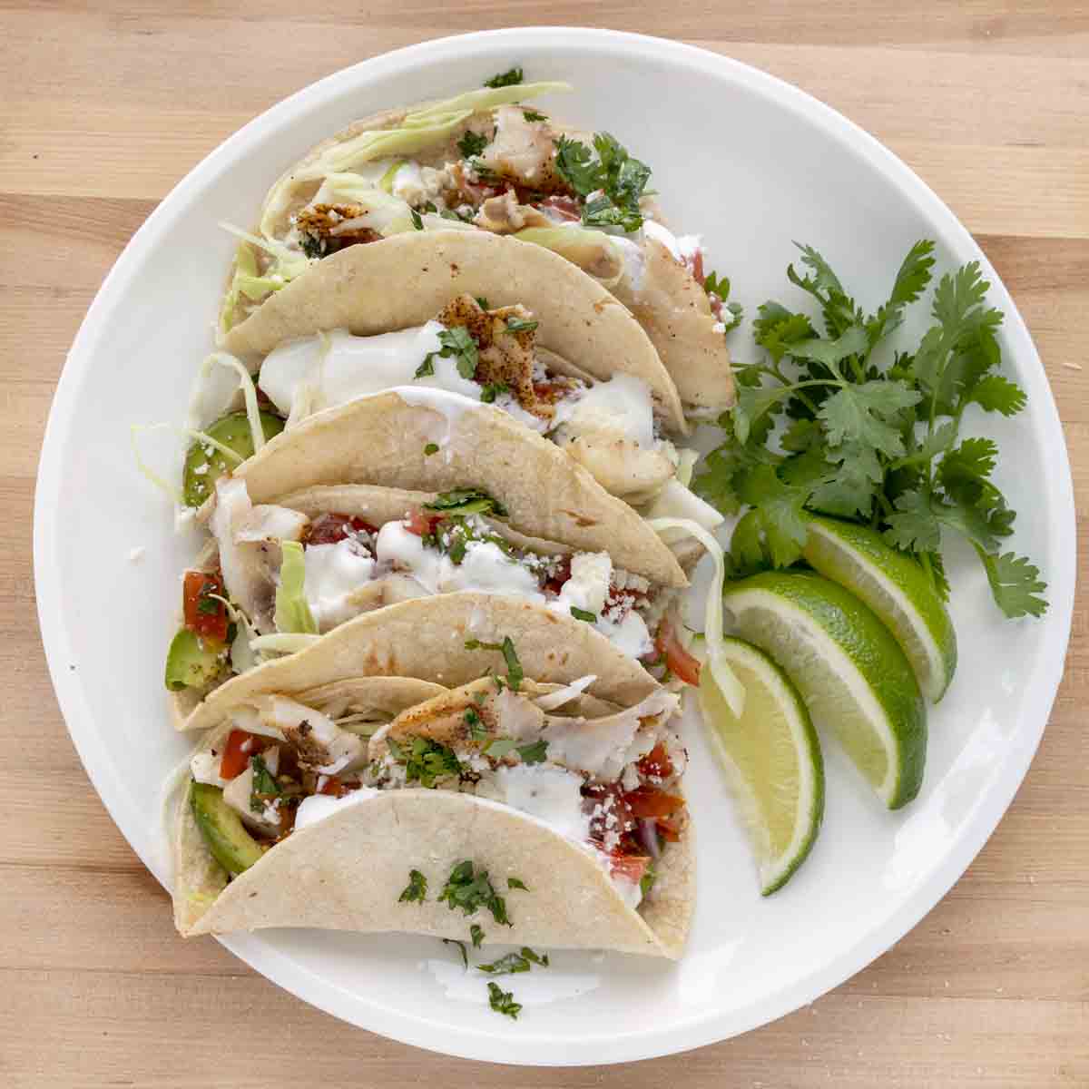 overhead view of 3 fish tacos with lime wedges on a white plate.