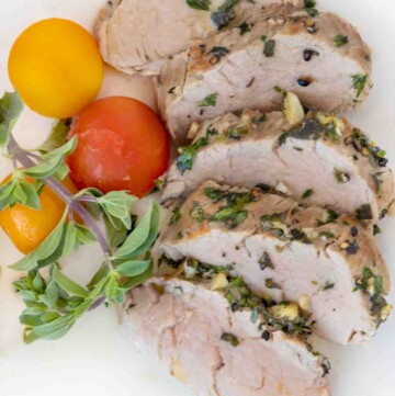 sliced garlic herb pork tenderloin fanned on a white plate with yellow and red cherry tomatoes