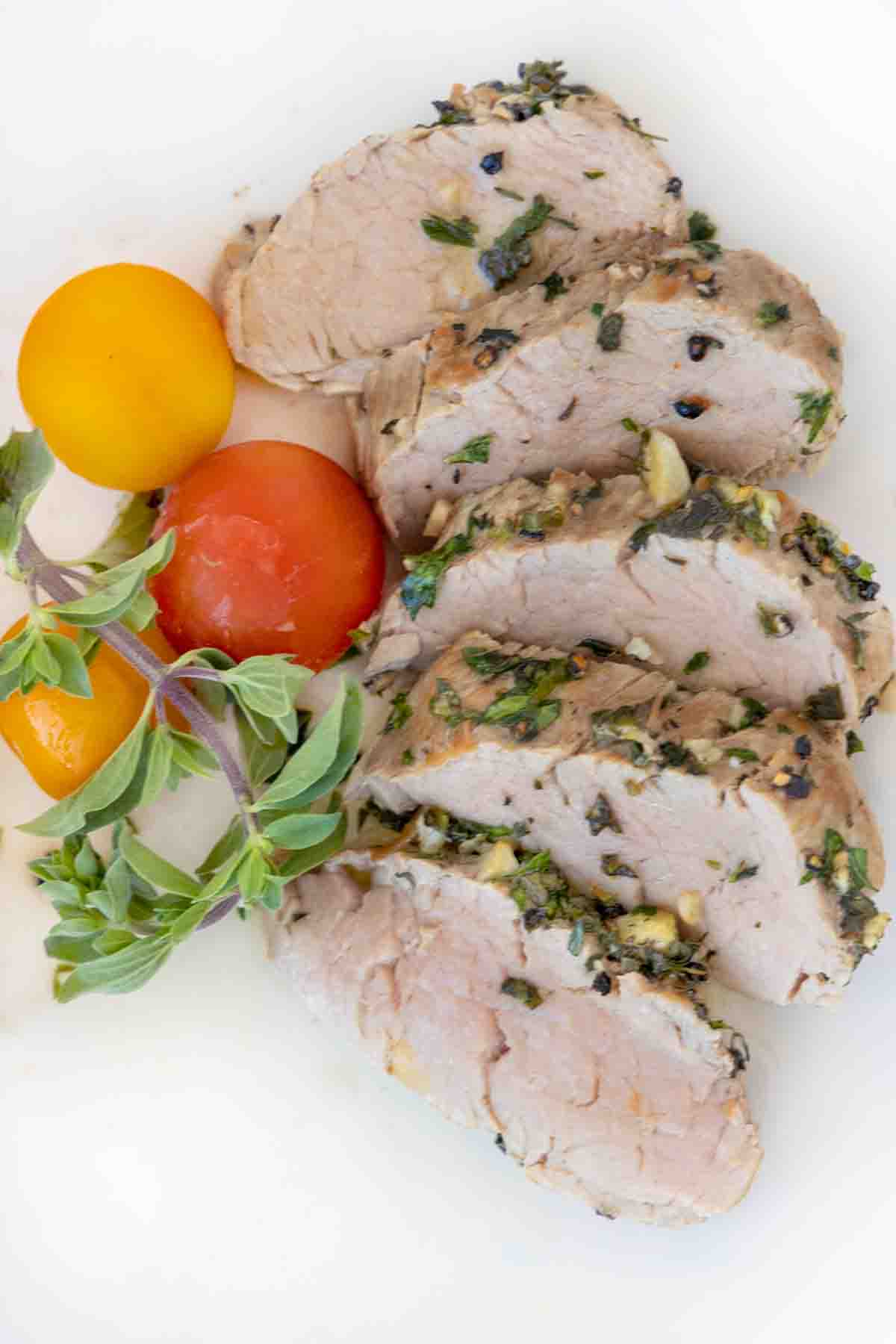 sliced garlic herb pork tenderloin fanned on a white plate with yellow and red cherry tomatoes