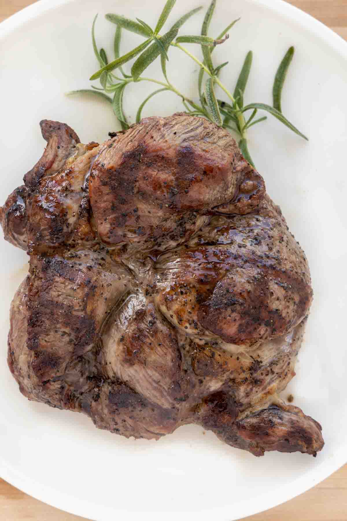 unsliced grilled leg of lamb on a white platter