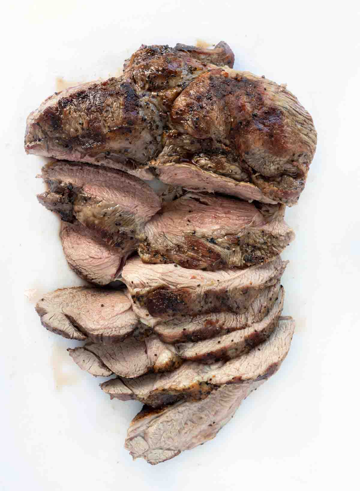 sliced grilled leg of lamb on a white platter