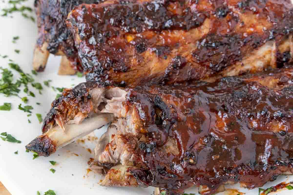 barbecued baby back ribs on a white platter with one of the bones pulled away from the rack