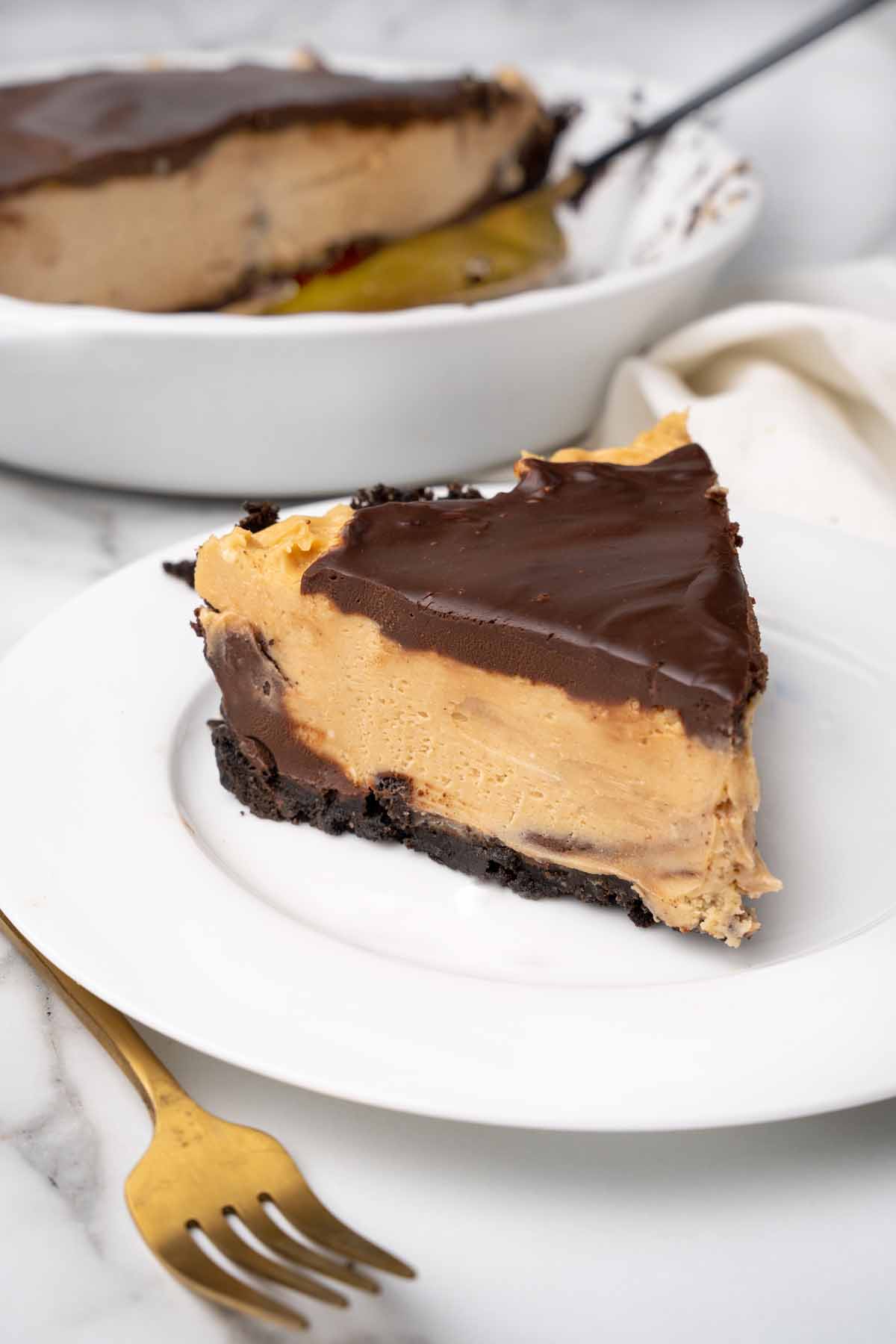 slice of peanut butter pie on a white plate with the rest of the pie behind it.