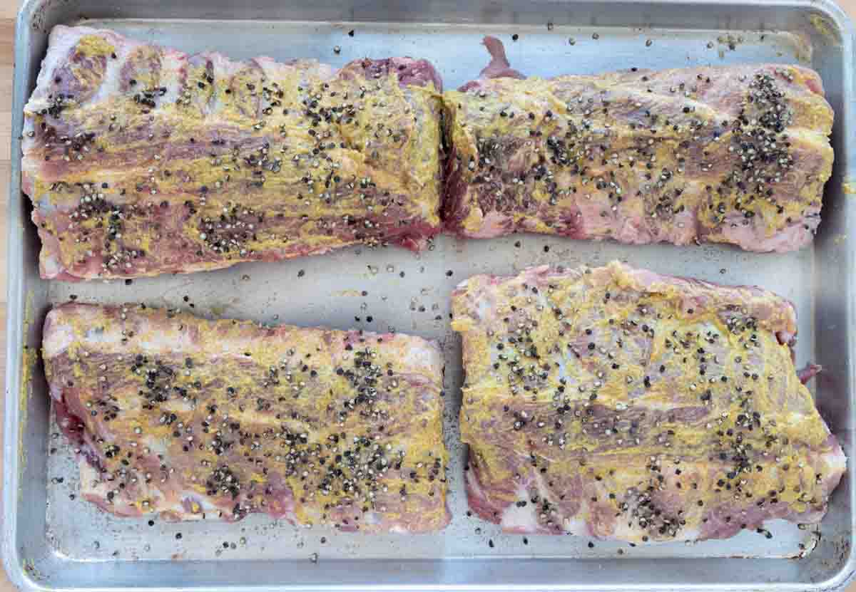four half racks of ribs coated with spicy mustard and seasoned with sea salt and black pepper