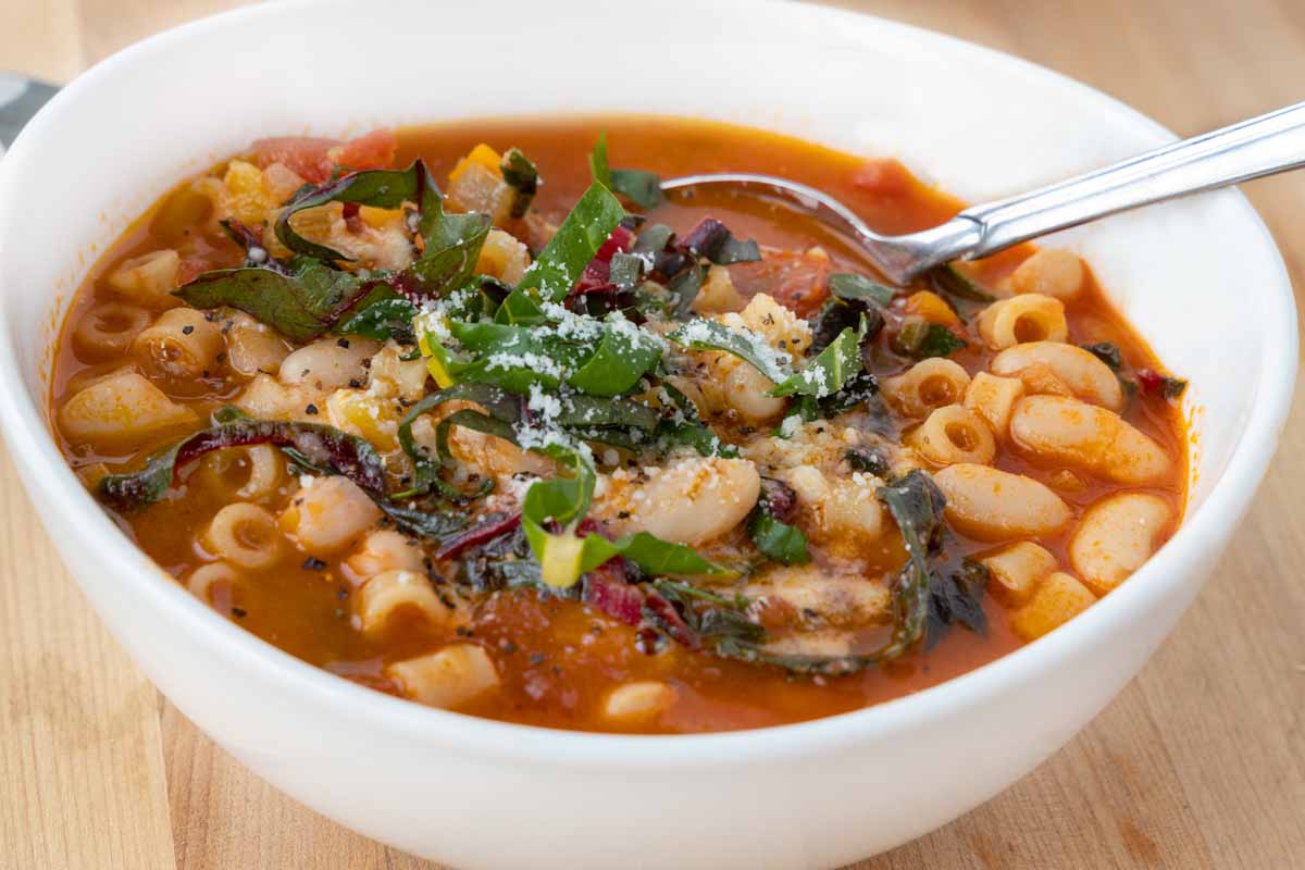 spoon in a white bowl filled with pasta fagioli