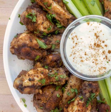 grilled cajun wings on white plate with bleu cheese dressing and celery sticks