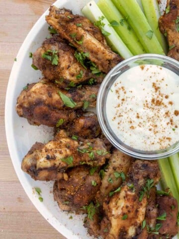 grilled cajun wings on white plate with bleu cheese dressing and celery sticks