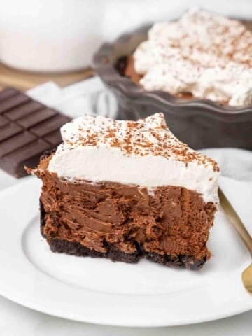 slice of chocolate silk pie on a white plate with the rest of the pie in the background