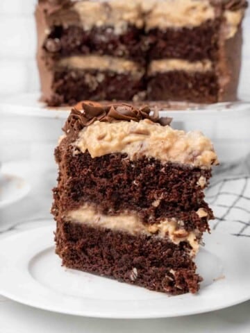 slice of German chocolate cake on a white plate with the whole cake in the background