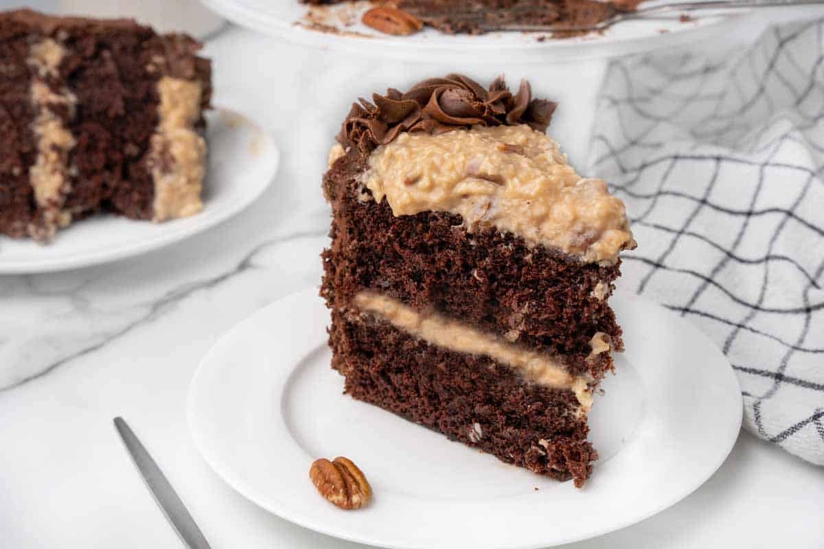 slice of german chocolate cake on a white plate with another slice in the background