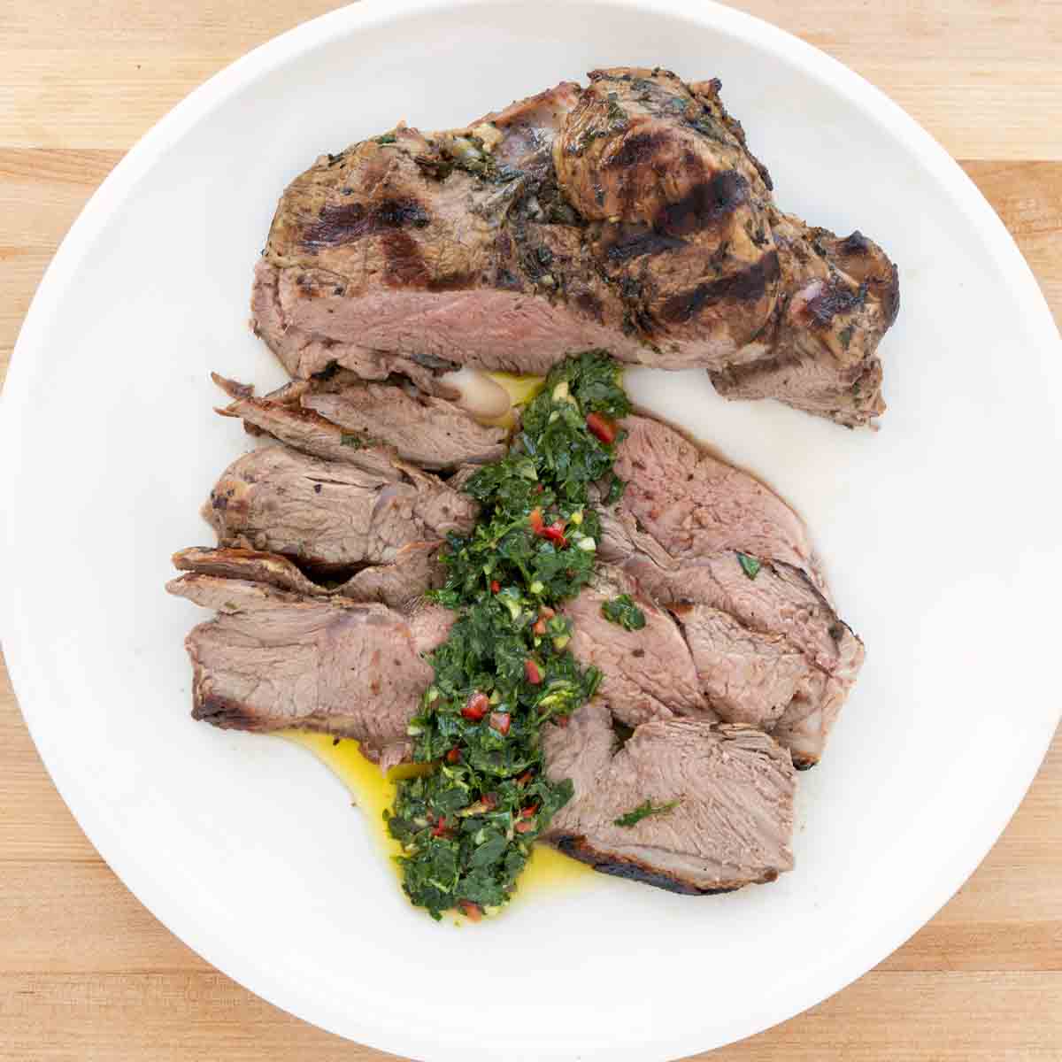 overhead sliced leg of lamb with chimichurri on a white plate