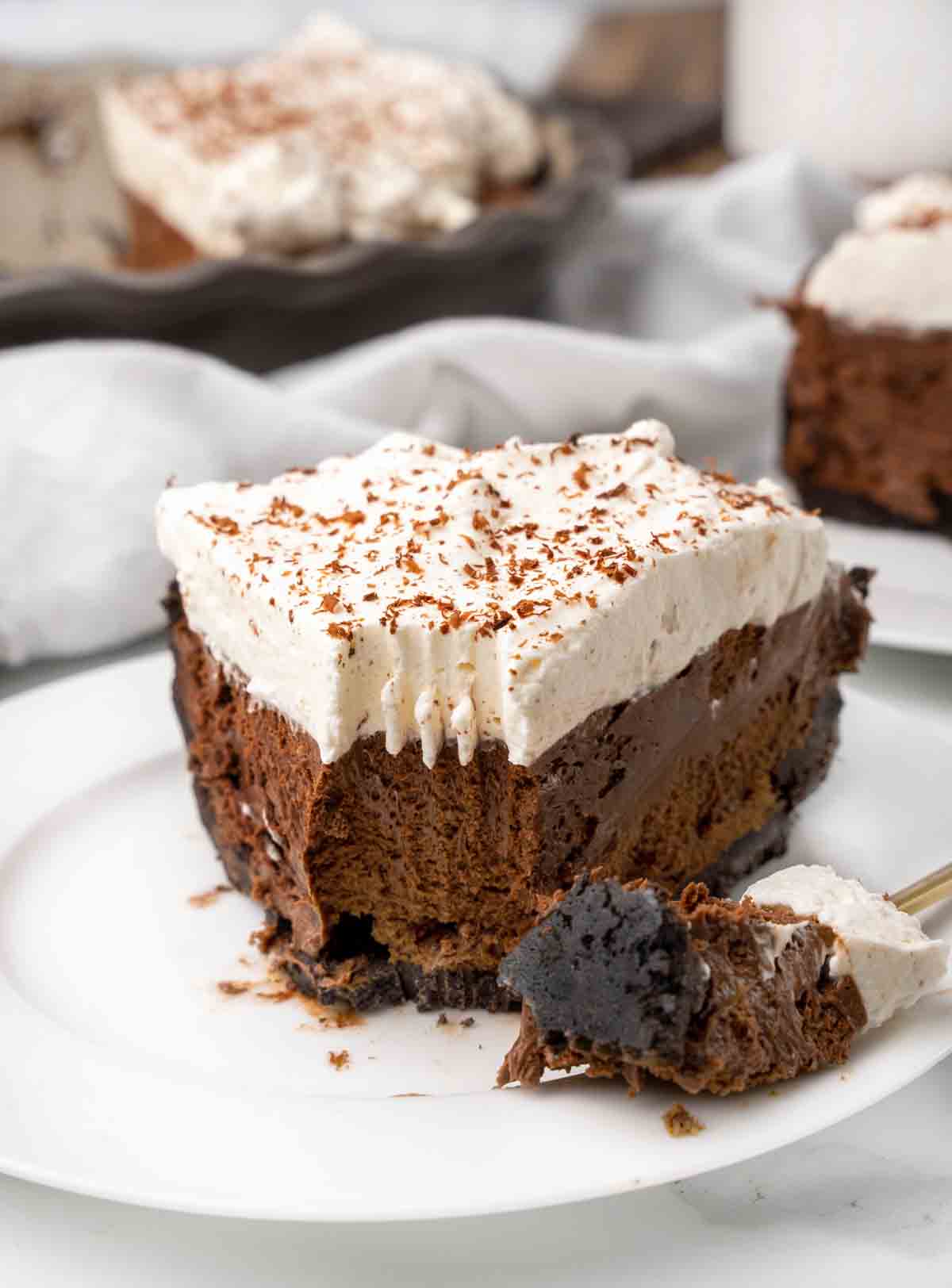 slice of chocolate silk pie on a white plate with a forkful of the pie on the side