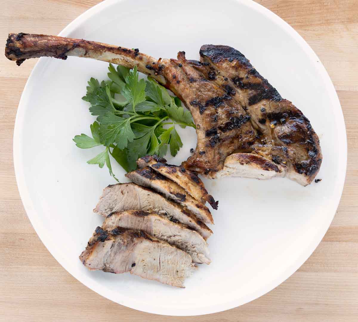 grilled pork chop sliced with slices fanned on a white plate