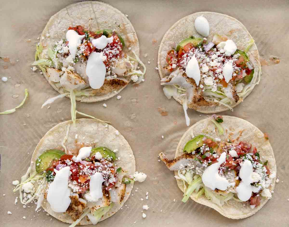 four tacos with toppings on a sheet pan