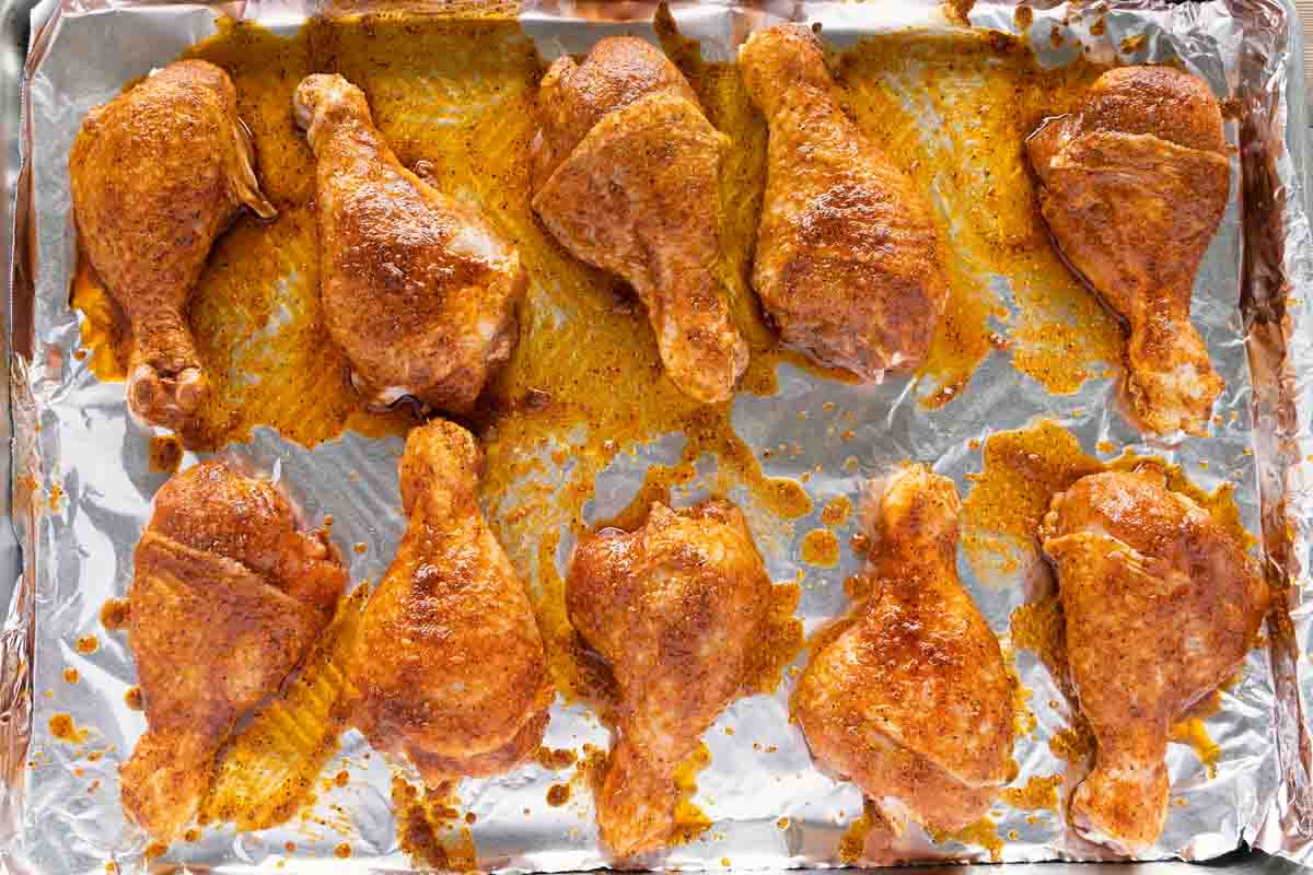 chicken legs coated with seasoning mixture on a foil lined baking tray