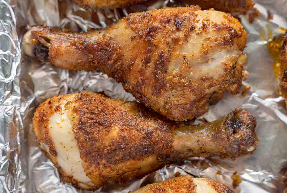 close up of seasoned crispy chicken legs on a foil wrapped tray