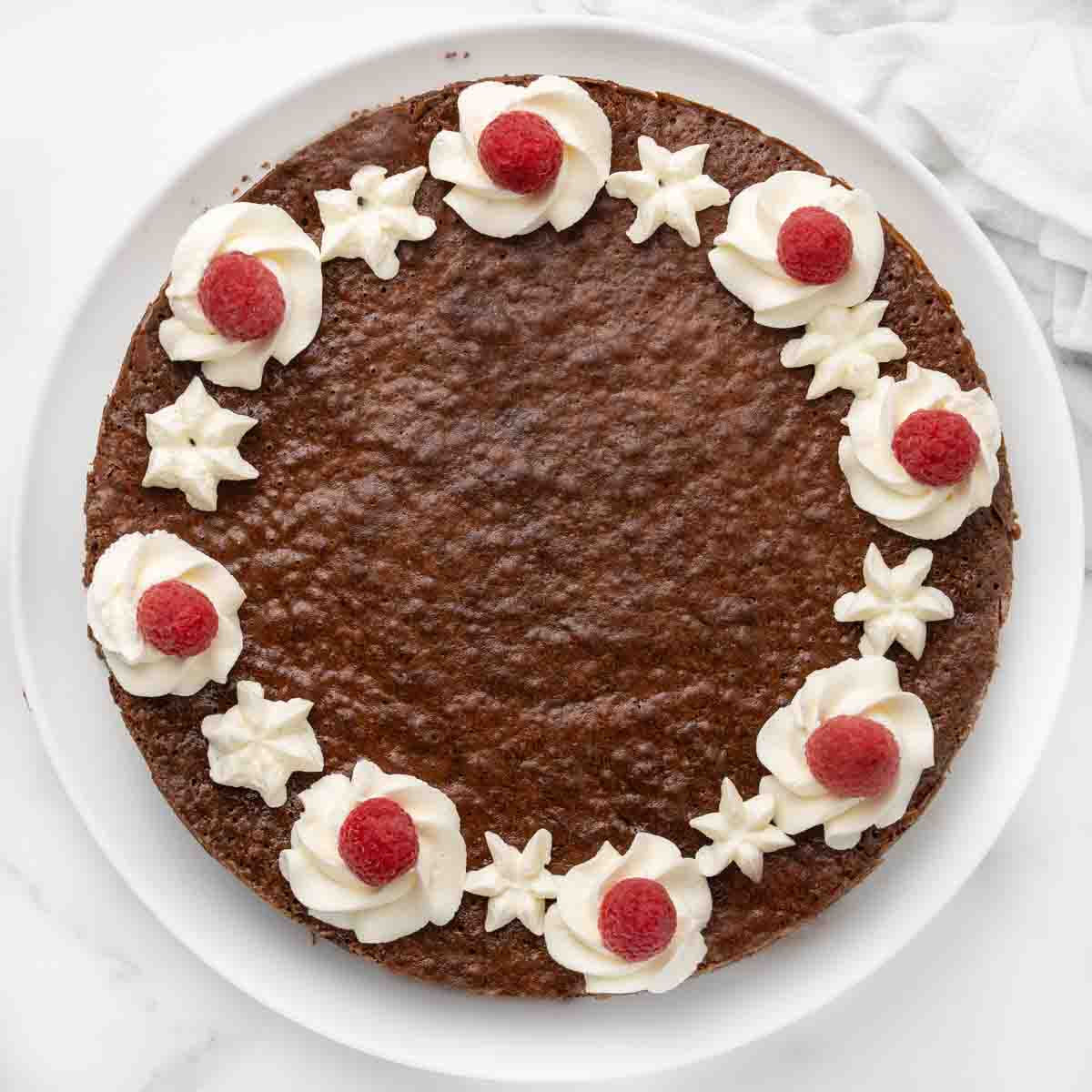 whole decorated flourless chocolate cake on a white platter