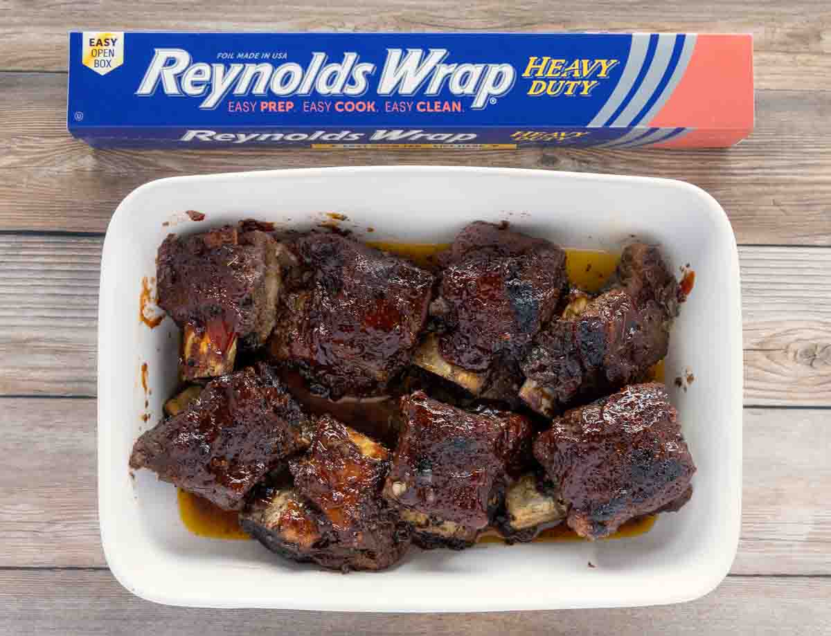Barbecued short ribs in a white casserole next to box of Reynolds foil