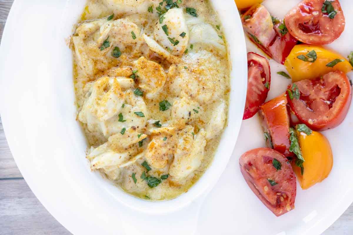 overhead partial view of seafood casserole and tomato salad on a white plate