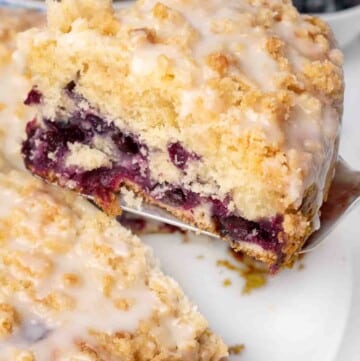 slice of blueberry coffee cake on a spatula being taken out of whole cake