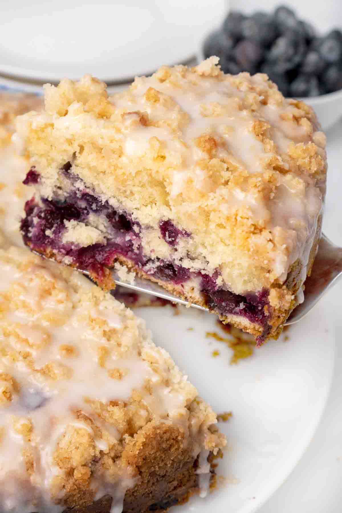 slice of blueberry coffee cake on a spatula being taken out of whole cake