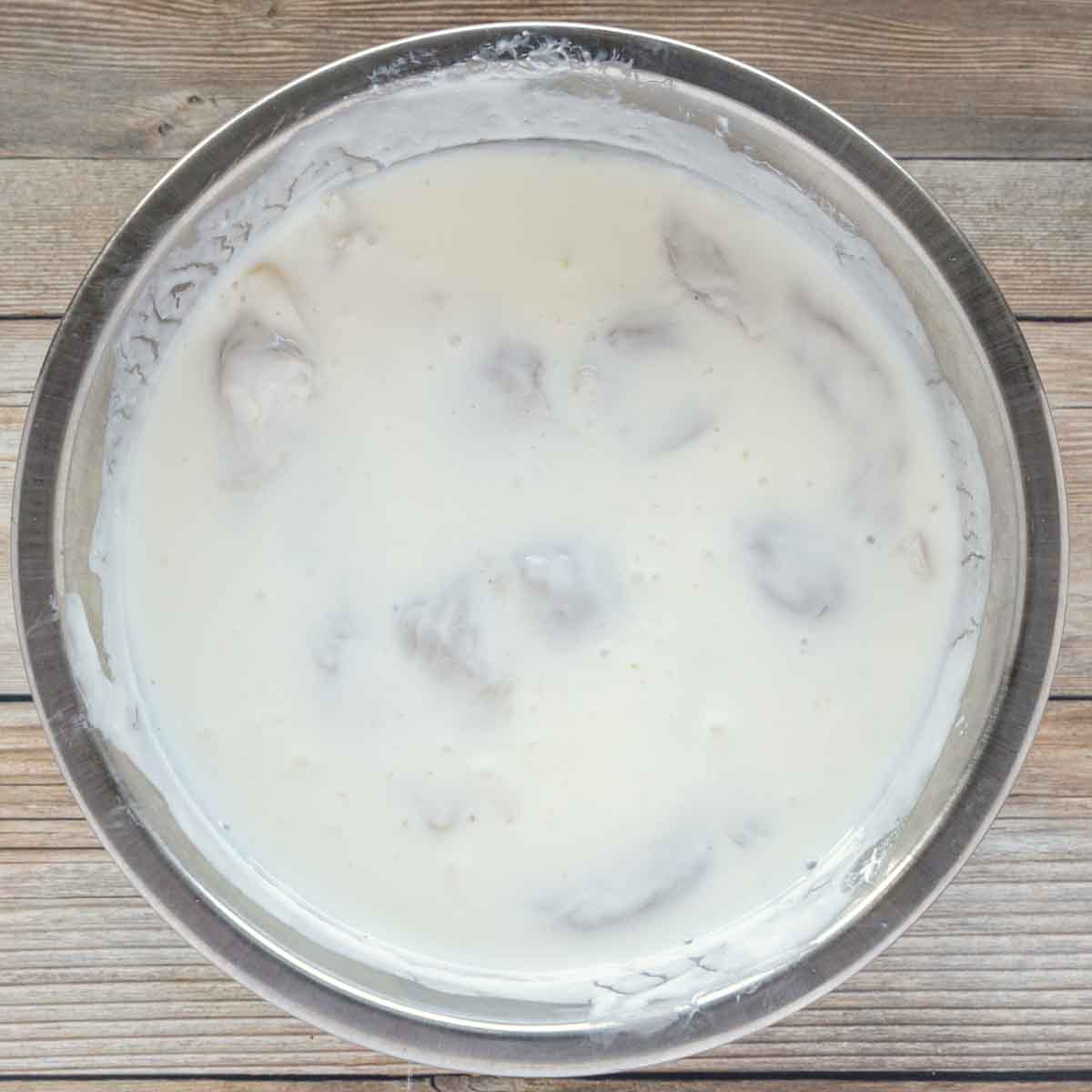 chicken tenders soaking in buttermilk in a stainless steel bowl