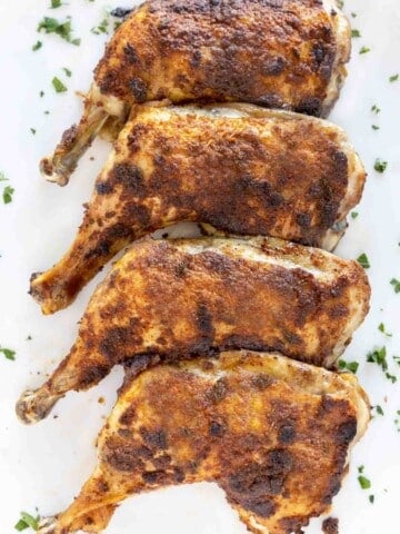 crispy seasoned chicken leg quarters on a white platter