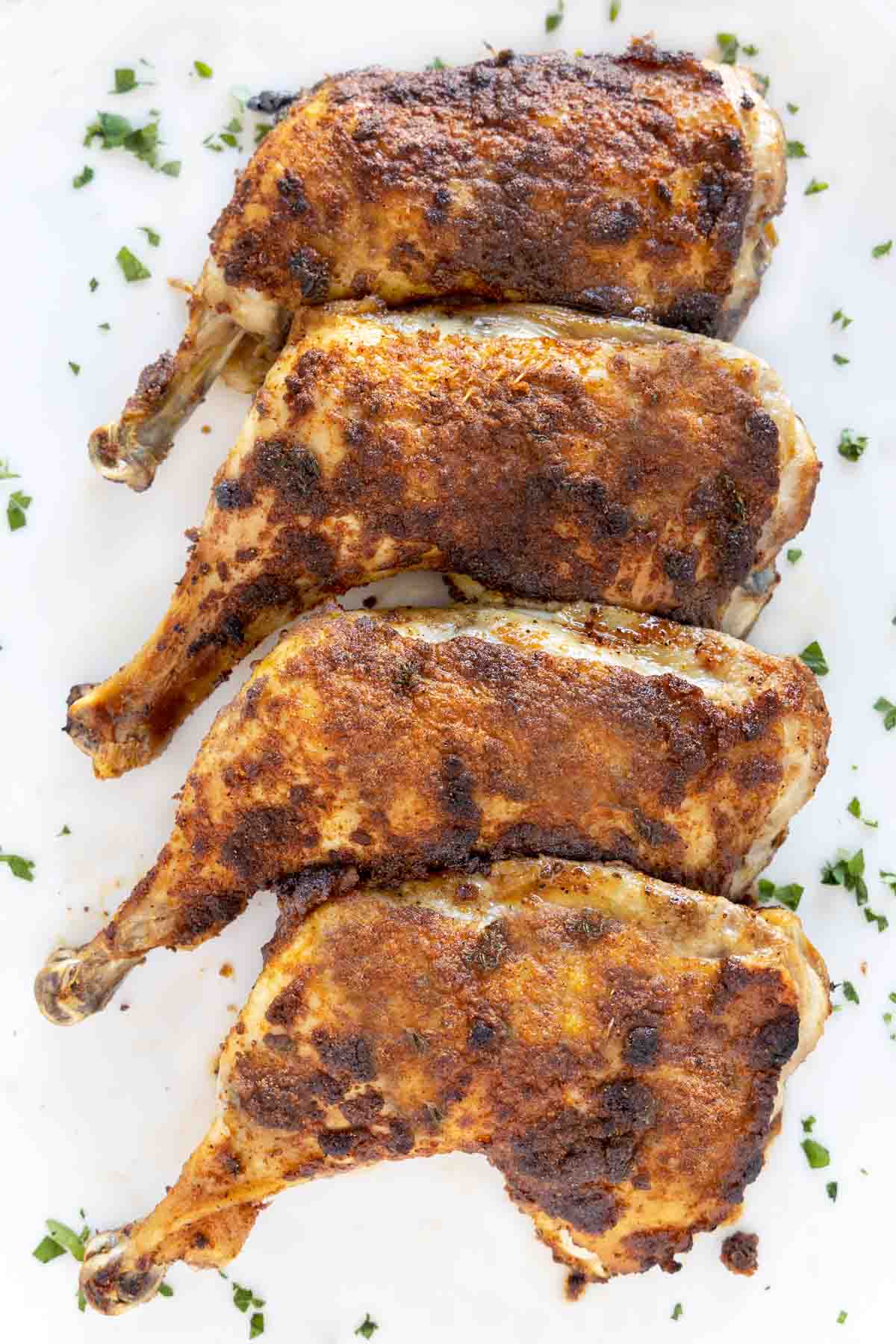 crispy seasoned chicken leg quarters on a white platter.