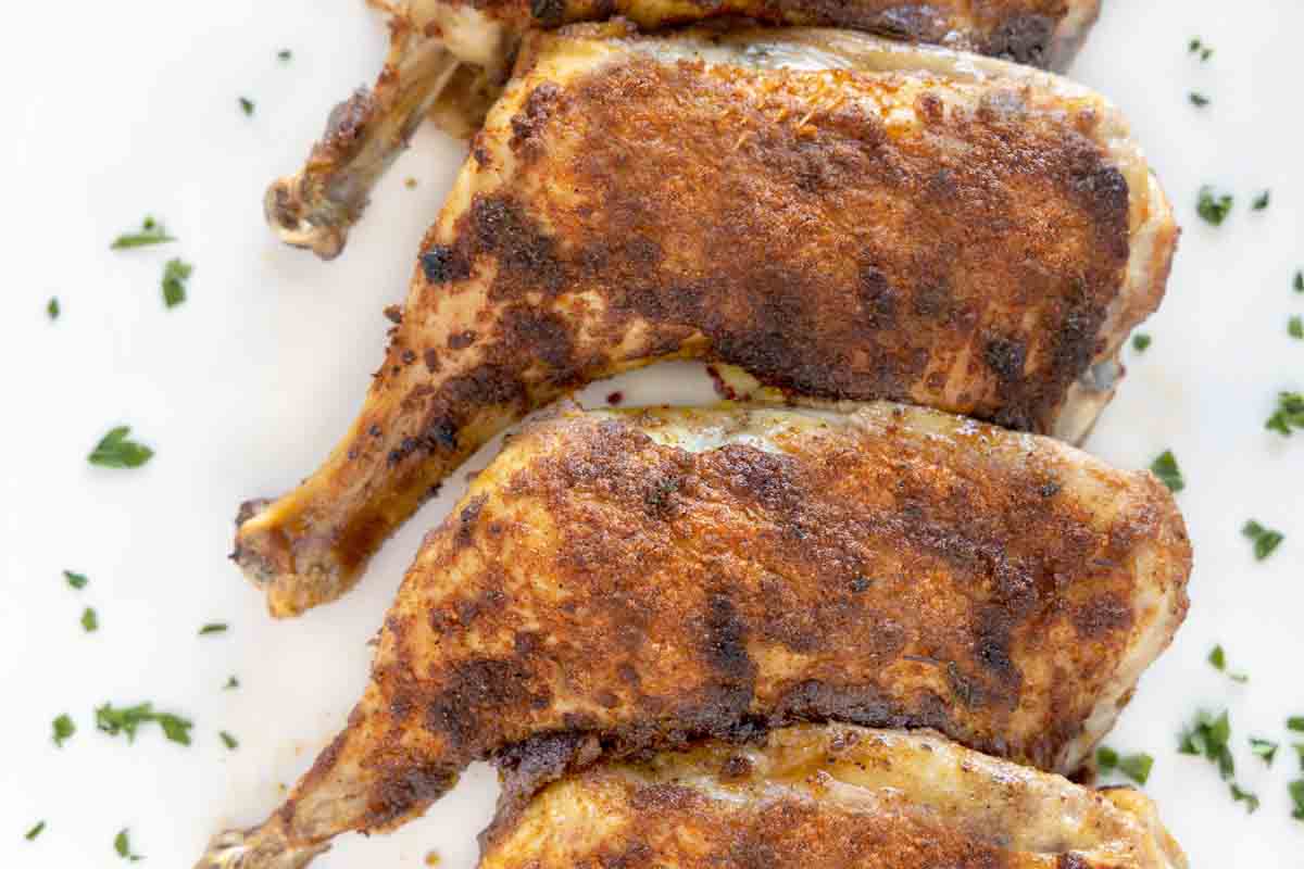 crispy seasoned chicken leg quarters on a white platter