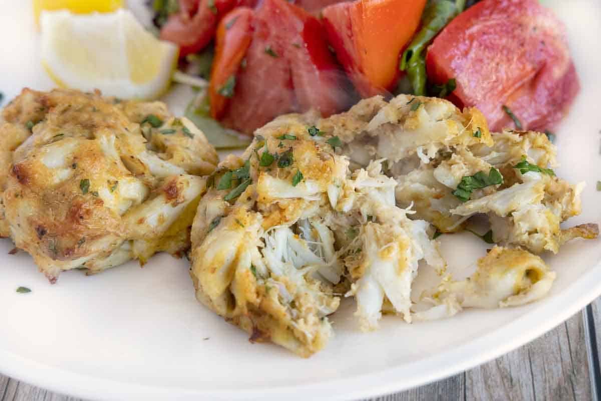 crab cake cut open showing inside on a white plate with tomatoes