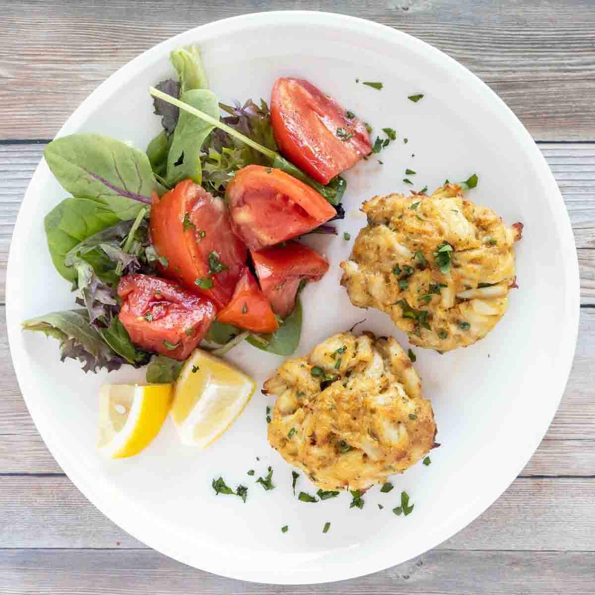 overhead shot of crab cakes on a white plate with tomato salad.