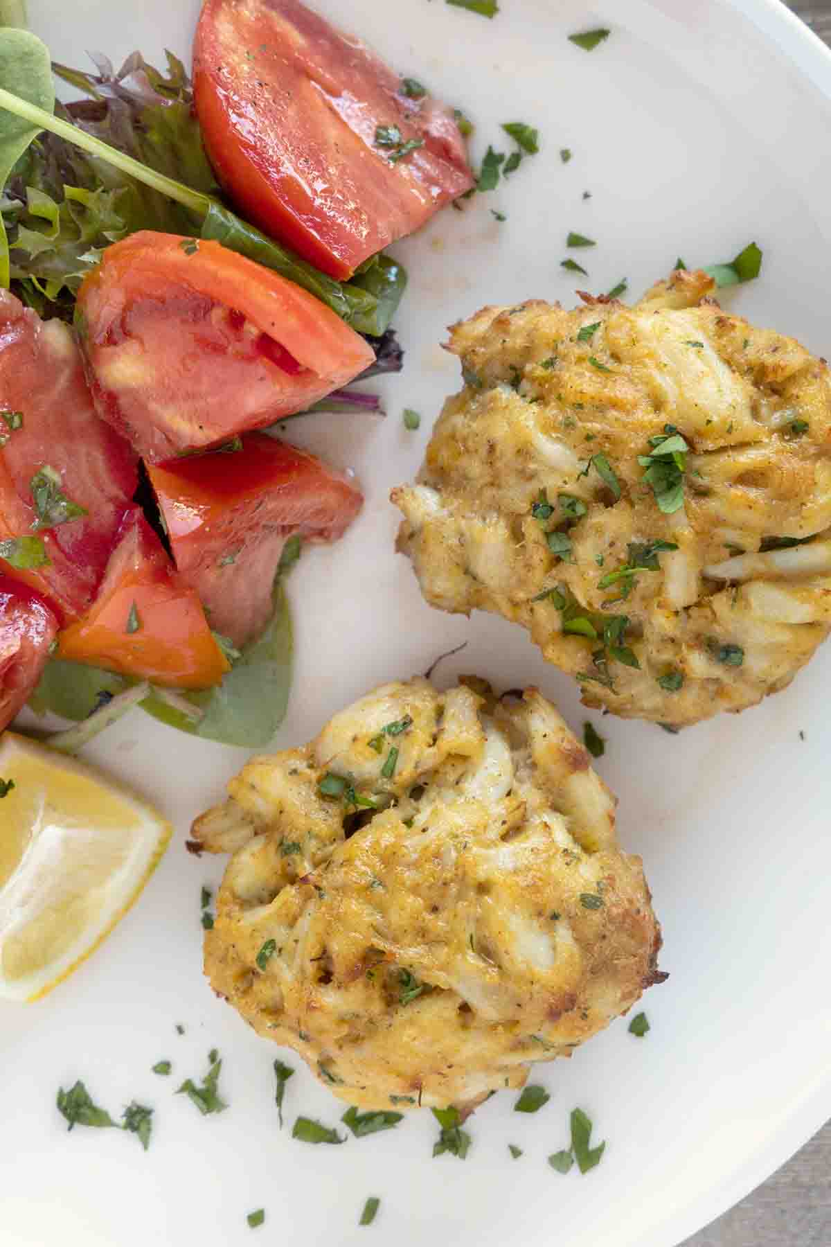 2 Maryland crab cakes with tomato salad on a white plate